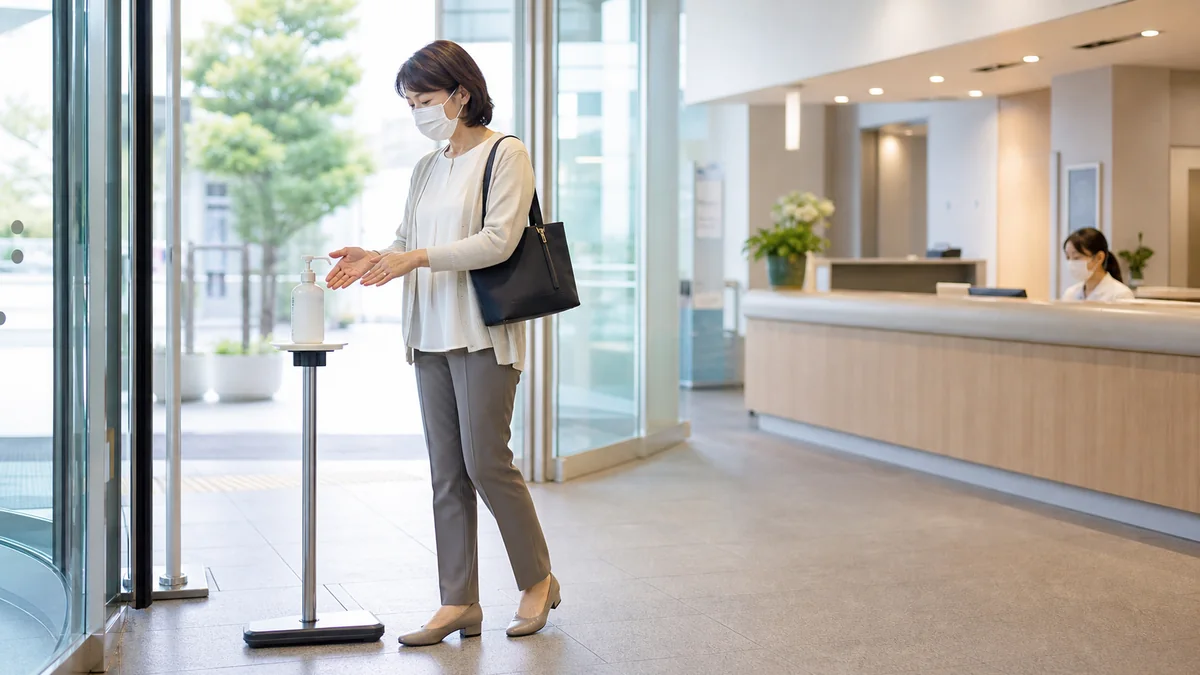 病院の面会受付でマスクと小さなバッグを持ち手指消毒をする女性